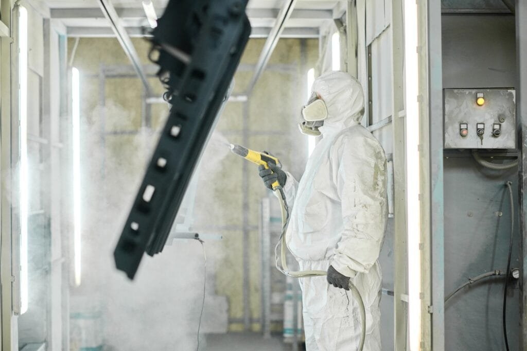 Technician using a spray gun to apply surface finishing on a metal part in Cast-Mold’s production facility.