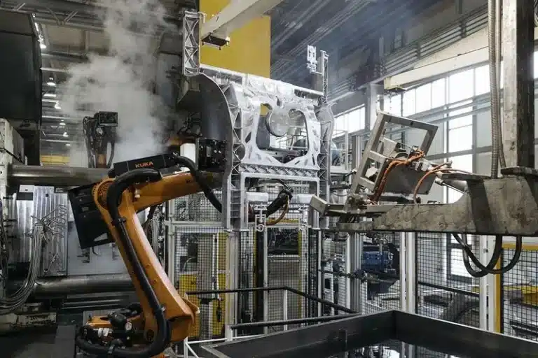 High pressure die casting cell with an industrial robot handling a large aluminum structural part amid steam in an automated factory.