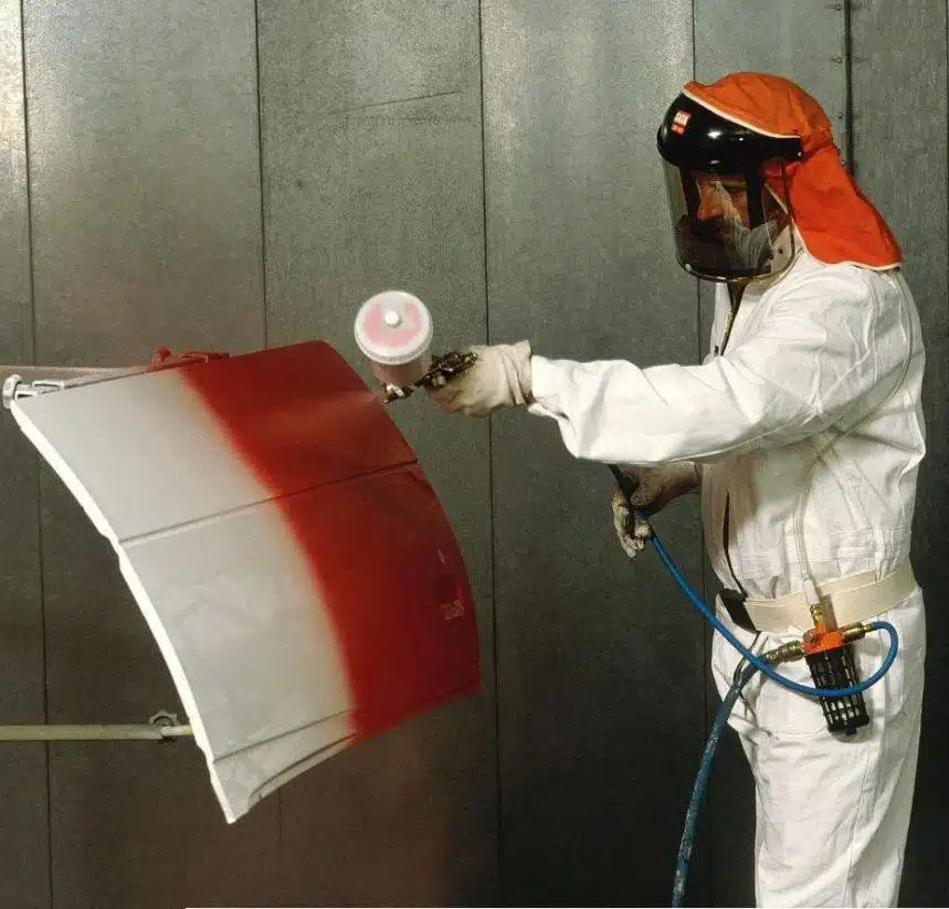 Operador pintando con aerosol un panel de metal con una capa roja como parte de un proceso de acabado de superficie industrial