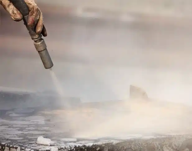 Boquilla de chorro abrasivo que limpia una superficie metálica con polvo y medios durante el granallado