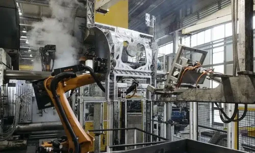 High pressure die casting cell with an industrial robot handling a large aluminum structural part amid steam in an automated factory.