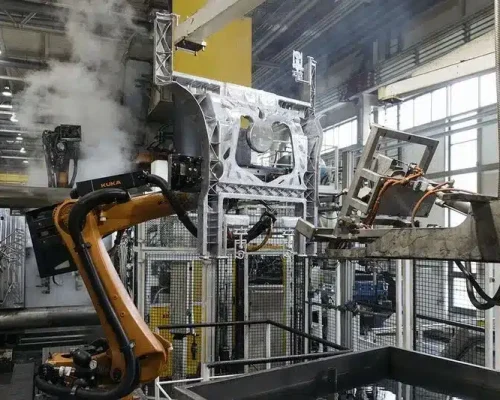High pressure die casting cell with an industrial robot handling a large aluminum structural part amid steam in an automated factory.