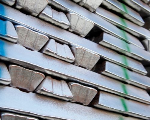 Stack of aluminum ingots on a pallet in a warehouse, ready to be melted as feedstock for aluminum die casting alloys.